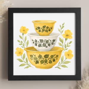 May include: A framed print featuring a stack of three vintage-style mixing bowls. The bowls are yellow and white with a black leaf and berry design. Yellow flowers and green leaves surround the bowls, set against a white background.