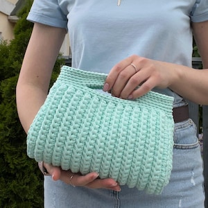 Handmade crochet clutch bag featuring a modern ribbed texture and minimalist design. Stylish crocheted purse made from chunky yarn, perfect for everyday wear, special occasions, and evening outings. The elegant rectangular shape adds a contemporary touch to any outfit. Detailed crochet stitches create a unique texture that makes this bag both fashionable and eye-catching.