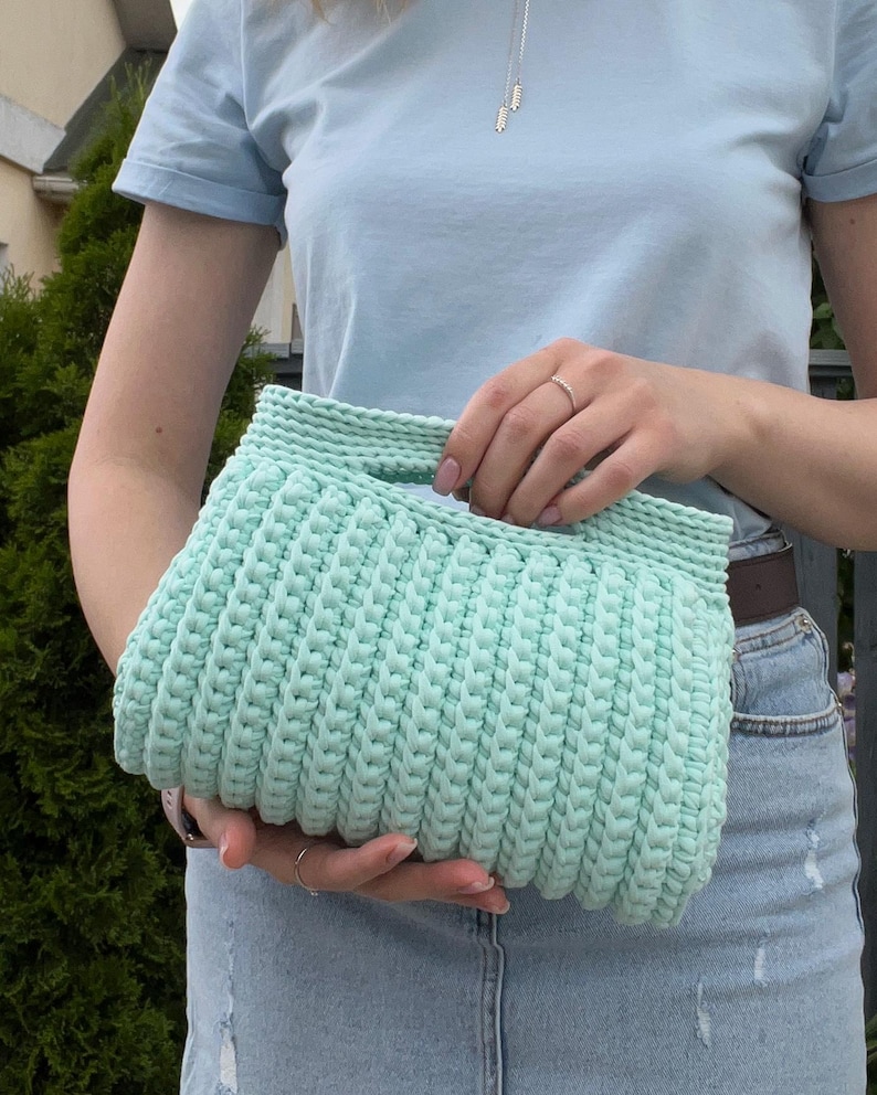 Handmade crochet clutch bag featuring a modern ribbed texture and minimalist design. Stylish crocheted purse made from chunky yarn, perfect for everyday wear, special occasions, and evening outings. The elegant rectangular shape adds a contemporary touch to any outfit. Detailed crochet stitches create a unique texture that makes this bag both fashionable and eye-catching.