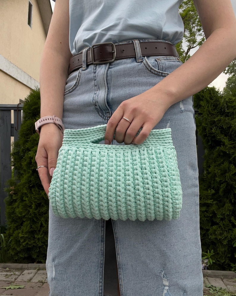 Handmade crochet clutch bag featuring a modern ribbed texture and minimalist design. Stylish crocheted purse made from chunky yarn, perfect for everyday wear, special occasions, and evening outings. The elegant rectangular shape adds a contemporary touch to any outfit. Detailed crochet stitches create a unique texture that makes this bag both fashionable and eye-catching.