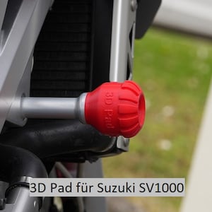 Może przedstawiać: Czerwony slider ramy motocyklowej z napisem "3D Pad". Slider jest przymocowany do srebrnej ramy motocyklowej. Pod sliderem widoczny jest napis "3D Pad für Suzuki SV1000".