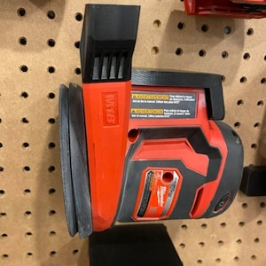 May include: A red and black Milwaukee power sander with a black sanding pad. The sander has a warning label in French, English, and Spanish. The sander is mounted on a pegboard.