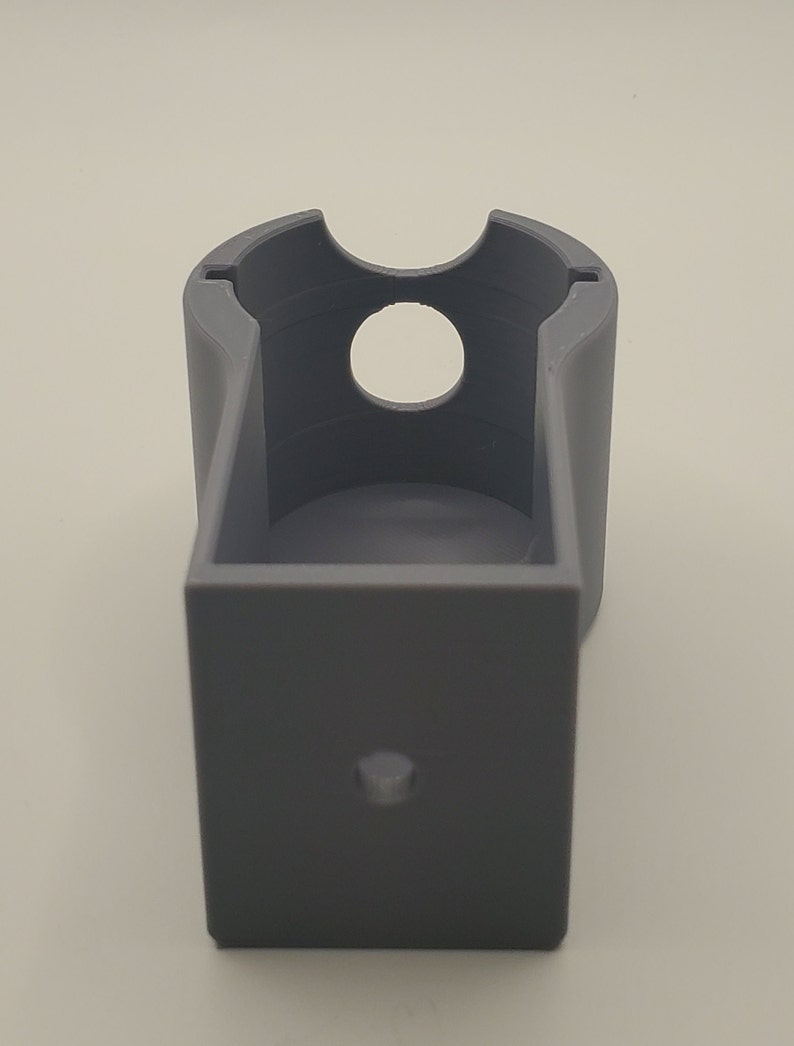 Puede incluir: Un soporte de pared de pl&aacute;stico gris impreso en 3D con una abertura circular para un dispositivo.