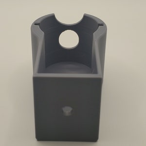 Puede incluir: Un soporte de pl&aacute;stico gris impreso en 3D con una abertura circular y un peque&ntilde;o agujero en la parte inferior.
