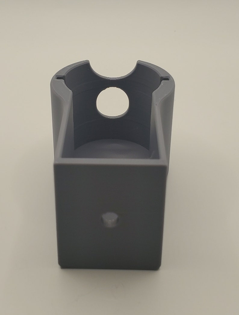 Puede incluir: Un soporte de pl&aacute;stico gris impreso en 3D con una abertura circular y un peque&ntilde;o agujero en la parte inferior.