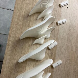 May include: Five white ceramic wall sconces with a unique, organic, mushroom-like design. Each sconce has a different size and shape, and they are all arranged in a row on a wooden surface. There are also five white plastic mounting plates.