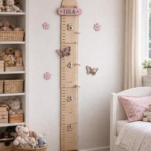 May include: A wooden growth chart with the name "ISLA" at the top. The chart measures up to 5 feet and features butterfly and flower decorations. The chart is mounted on a white wall in a child's bedroom.