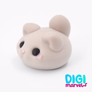Puede incluir: Una figura redondeada de color beige claro impresa en 3D que representa a una criatura con grandes ojos negros, orejas peque&ntilde;as y detalles rosados en las mejillas y la nariz. El texto DIGI marvels aparece en azul y magenta abajo a la derecha.
