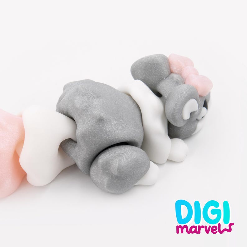 K&ouml;nnte beinhalten: Eine kleine, modellierte Tierfigur in Grau mit einem wei&szlig;en Kragen und einer hellrosa Schleife auf dem Kopf. Die Figur liegt und hat eine glatte, matte Textur. Der Text "DIGI marvels" ist in Blau und Pink in der unteren Ecke aufgedruckt.