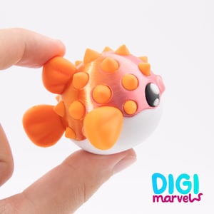 May include: A small, spherical pufferfish figurine featuring a gradient orange and pink body with protruding orange spikes, orange fins, and a white underbelly. The fish has a large black eye with white highlights and the text DIGI marvels.