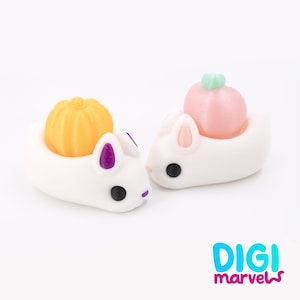 May include: Two white bunny figurines with black eyes and colorful accents. One bunny has a yellow pumpkin on its back, and the other has a pink peach with a green stem. The logo "DIGI marvels" is in the bottom right corner.