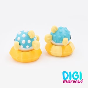 May include: Two small pufferfish figurines in yellow inflatable rings. The pufferfish are light blue with white polka dots and yellow fins. The text DIGI marvels is printed in the bottom right corner in a bright blue and magenta font.