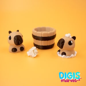 May include: An orange background showcases three small, tan capybara figurines with black details, a small barrel, and a white object. The capybaras have black noses and ears. The barrel is tan with black bands. The text "DIGIS marvel" is in the bottom right.