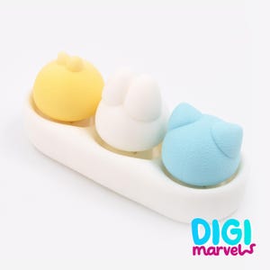 May include: A white ceramic tray holds three colourful, animal-shaped sponges. A yellow chick, a white bunny, and a blue cat are arranged in a row. The text "DIGI marvels" is in the bottom right corner.