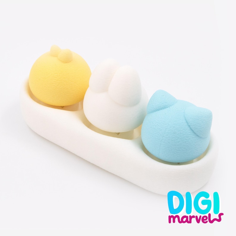 May include: A white ceramic tray holds three colourful, animal-shaped sponges. A yellow chick, a white bunny, and a blue cat are arranged in a row. The text "DIGI marvels" is in the bottom right corner.