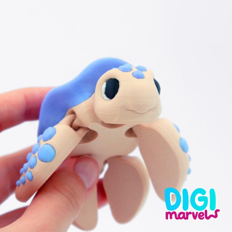 May include: A 3D-printed toy turtle with a light blue shell and accents, and a tan body. The turtle has large black eyes and is held in a hand. The text "DIGI marvels" is visible in the lower right corner.