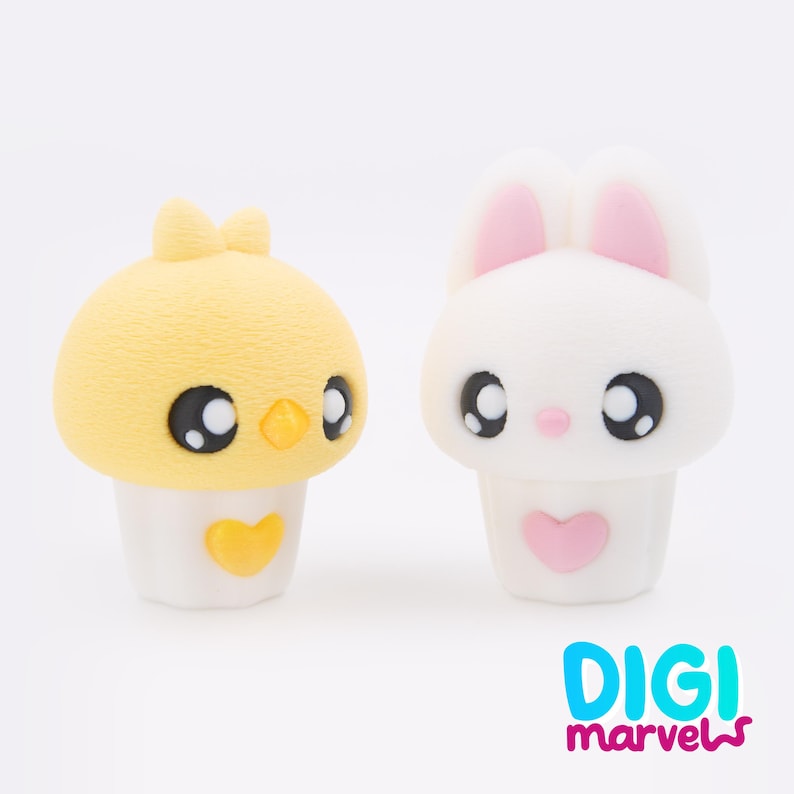 May include: Two cute cartoon figures: a yellow chick with a bow and a white bunny with pink ears. Both have large black eyes and are set on a white base with a heart. The text "DIGI marvels" is at the bottom.