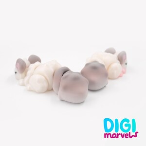 K&ouml;nnte beinhalten: Drei kleine, stilisierte Tierfiguren in einer Reihe mit glatten, matten Oberfl&auml;chen in Creme- und sanften Graut&ouml;nen. Jede Figur hat abgerundete Ohren und ein minimalistisches Design. Der Text "DIGI marvels" ist unten rechts zu sehen.