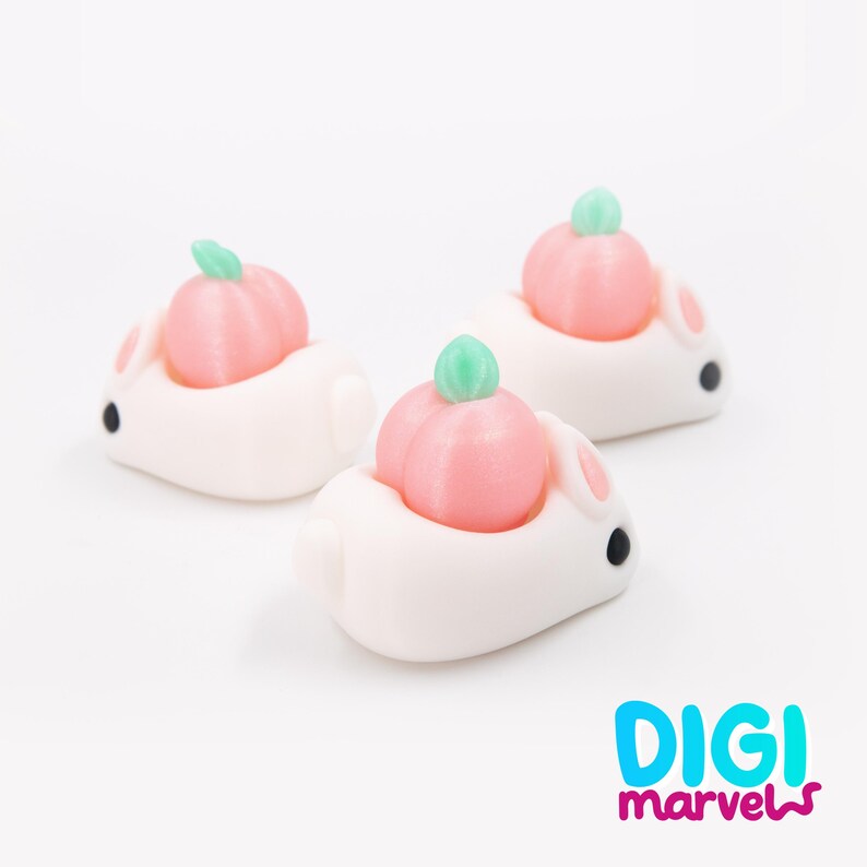 May include: Three white bunny figurines, each with a pink pumpkin on its back. The pumpkins have green stems. The bunnies have black eyes and pink inner ears. The figurines are on a white background.