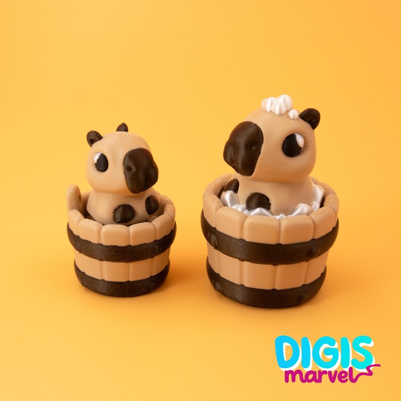 May include: Two tan and brown capybara figurines in wooden tubs with dark brown stripes. One has a white fluffy accent on its head. The background is a solid orange color. The text "DIGIS marvel" is in the bottom right corner.