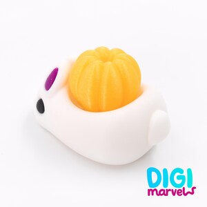May include: A white bunny-shaped container with a bright orange pumpkin inside. The bunny has purple ears and a black eye. The image has the text "DIGI marvels" in the bottom right corner.