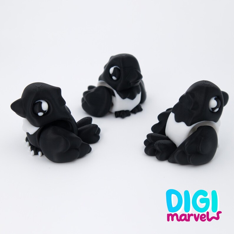 Peut inclure: Trois petites figurines d'oiseaux stylis&eacute;es en noir et blanc, chacune dot&eacute;e de grands yeux expressifs et d'une apparence arrondie rappelant un dessin anim&eacute;. Le texte "DIGI marvels" est imprim&eacute; en bas &agrave; droite dans une police bleu et rose.