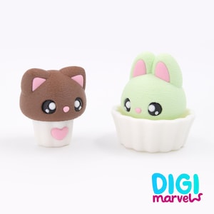 May include: Two cute figurines: a brown cat with pink details and a green bunny with pink ears. The cat has a white base with a pink heart, and the bunny sits in a white cupcake case. The Digi Marvels logo is in the bottom right.