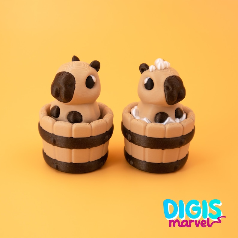 May include: Two tan and black capybara figurines in wooden tubs. The capybaras have black ears and noses, with black spots on their bodies. One has white foam around it. The tubs have dark brown bands. The background is yellow.