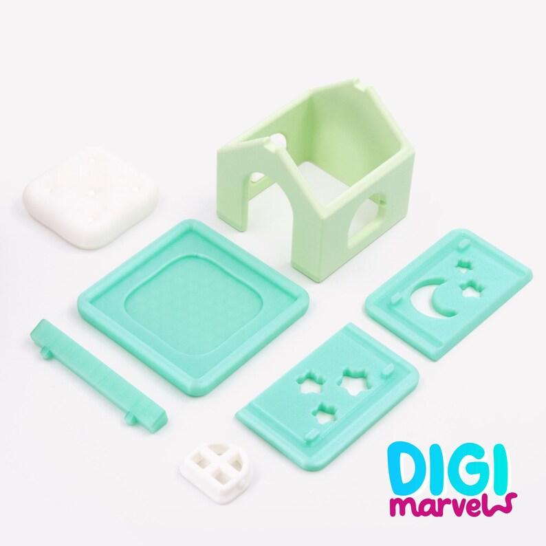 Pode incluir: Um conjunto de casa de brinquedo desmontado com uma estrutura de casa verde-clara, uma base quadrada branca, uma plataforma quadrada azul-petr&oacute;leo, um painel retangular com recortes de lua e estrelas e uma pequena pe&ccedil;a de janela branca.