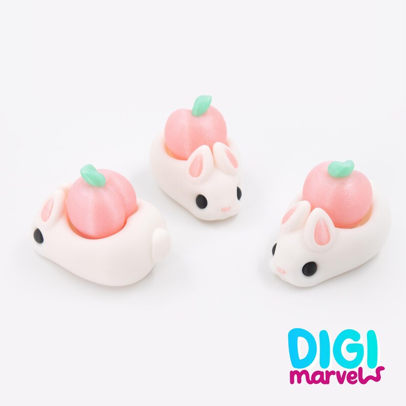 May include: Three white bunny figurines, each with a pink pumpkin on its back. The bunnies have pink inner ears, black eyes, and a small tail. The pumpkins are light pink with green stems. The Digi Marvels logo is in the bottom right corner.