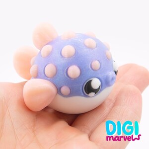 May include: A small, spherical pufferfish figurine featuring a shimmering purple body with raised, light pink polka dots. It has smooth, light pink fins and a white underbelly. The eyes are large, black, and white. The text DIGI marvels is visible.
