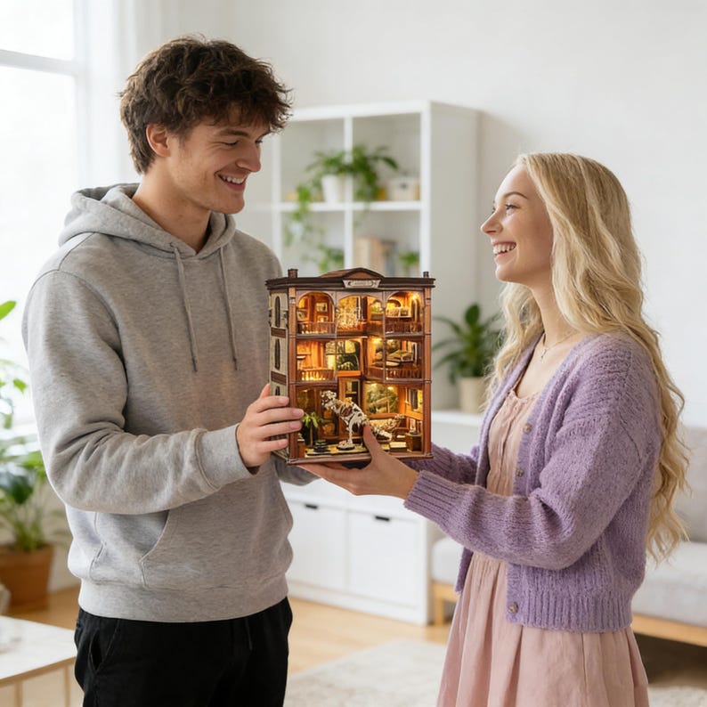 Op de afbeelding: Een gedetailleerd miniatuurpoppenhuis met binnenverlichting. De meerlaagse structuur heeft een bruine gevel met architectonische details. Het interieur is gemeubileerd en bevat een klein hondenbeeld. Het poppenhuis wordt door twee personen vastgehouden.