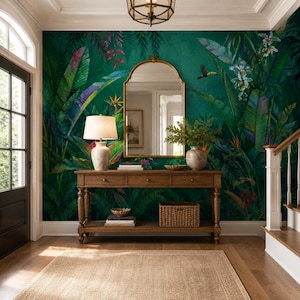 May include: A wooden console table with three drawers and a lower shelf sits against a wall covered in dark green tropical wallpaper featuring large leaves, flowers, and a toucan. An arched mirror, a lamp, and a woven basket are on the table.