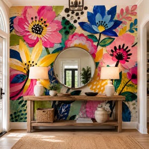 Puede incluir: Una mesa consola de madera con una cesta tejida, dos lámparas y un jarrón de cerámica, colocada contra una pared con un gran mural floral colorido con pétalos rosas, amarillos y azules, centrado por un espejo redondo que refleja una puerta.