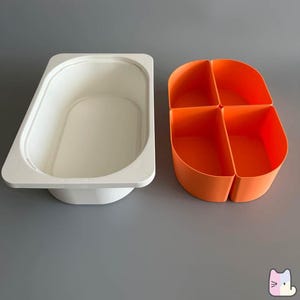 May include: Two-piece plastic storage containers. One is a white rectangular container with rounded corners. The other is an orange container divided into four sections. Both containers are on a gray background.