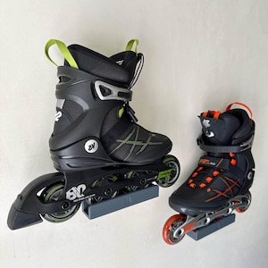 Peut inclure: Deux patins à roulettes en ligne, un grand et un petit, sont présentés contre un mur blanc. Le grand patin est noir avec des détails verts, et le petit est noir avec des accents orange. Les deux ont plusieurs roues.