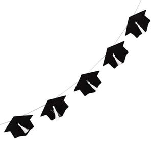 May include: A banner of black graduation caps, each with a white tassel, strung together on a silver string. This decorative garland is designed for graduation celebrations. The caps are set against a plain white background.