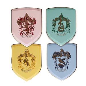 Puede incluir: Cuatro platos de papel en forma de escudo con los escudos de las casas de Hogwarts: Gryffindor, Slytherin, Hufflepuff y Ravenclaw. Cada plato tiene un fondo de color diferente y un borde dorado. Gryffindor es rosa, Slytherin es verde azulado, Hufflepuff es amarillo y Ravenclaw es azul claro.