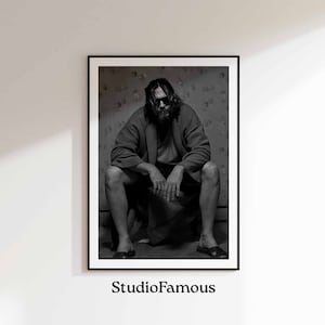 May include: Black and white photograph of a man wearing sunglasses and a robe, sitting on a toilet. The man has a beard and long hair. The photo is in a black frame.