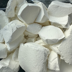 May include: A close-up of a white, powdery substance in a plastic bag. The substance is broken into irregular chunks.