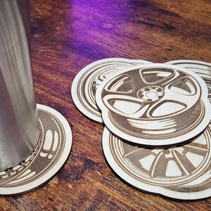May include: Set of five brown wooden coasters with a laser-etched design of a car wheel. The coasters are round and have a slightly raised edge.
