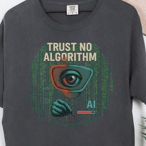 May include: Dark gray t-shirt with the text "TRUST NO ALGORITHM" above a graphic of an eye within a circuit board design. The graphic includes the letters "AI" and a hand. The shirt is hanging on a wooden hanger.