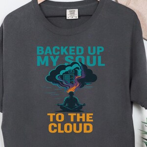 May include: Dark grey t-shirt with the text "BACKED UP MY SOUL TO THE CLOUD" in teal and orange. The graphic features a person meditating with a cloud and data center design above their head.