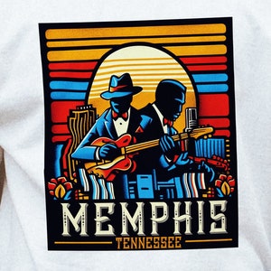 Pode incluir: Camiseta branca com uma estampa gráfica de dois músicos tocando instrumentos em frente a um pôr do sol com o texto "Memphis Tennessee" abaixo.
