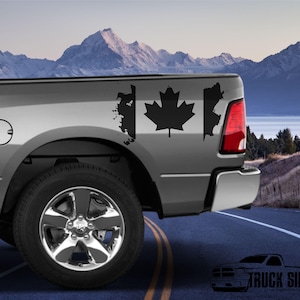 Puede incluir: Una calcomanía de bandera canadiense en blanco y negro en el lateral de una camioneta gris. La calcomanía tiene la forma de la bandera canadiense con una hoja de arce en el centro.