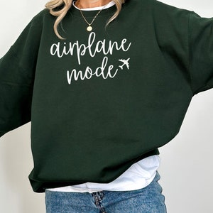 May include: A dark green sweatshirt with the words "airplane mode" in white script, along with a small airplane graphic. The sweatshirt is a casual style, suitable for travel or everyday wear.
