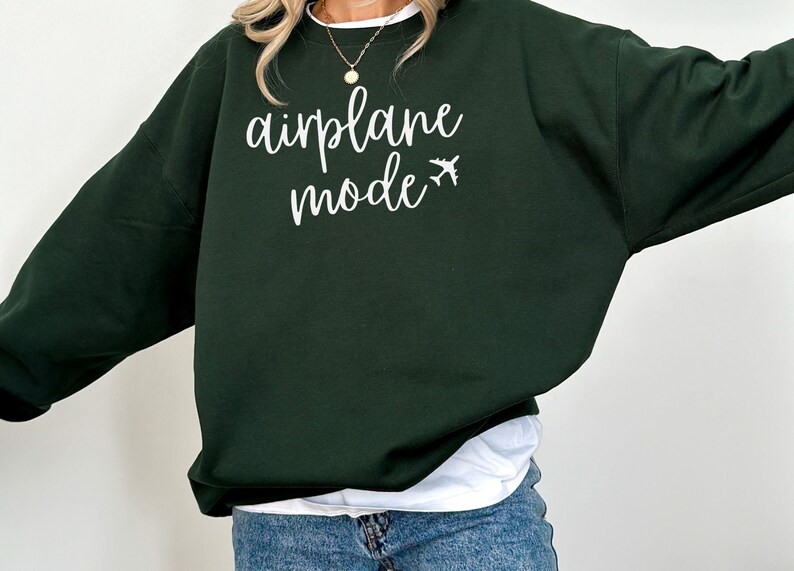 May include: A dark green sweatshirt with the words "airplane mode" in white script, along with a small airplane graphic. The sweatshirt is a casual style, suitable for travel or everyday wear.