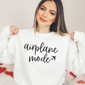 May include: White sweatshirt with the words "airplane mode" in a black script font, along with a small airplane graphic. The sweatshirt is a long-sleeved crew neck.