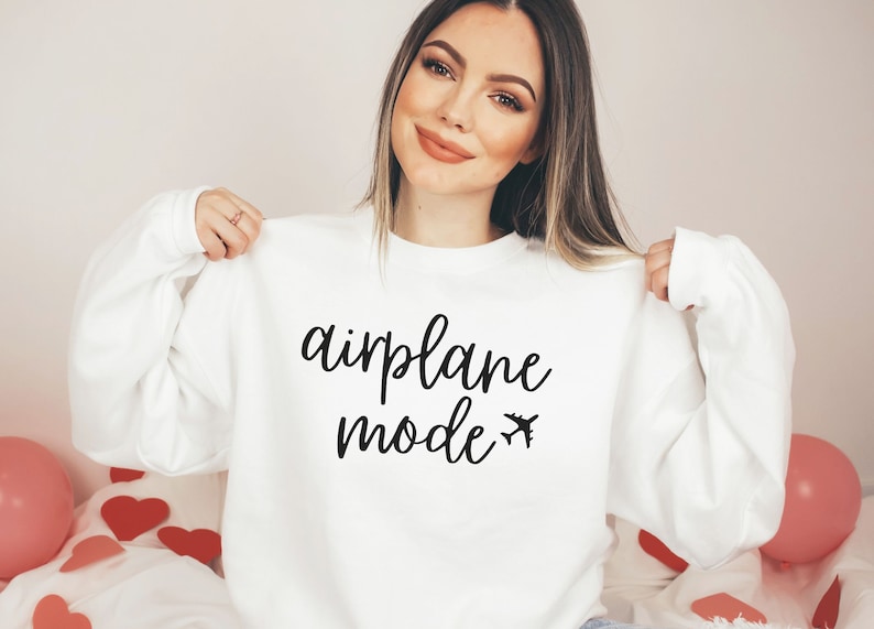 May include: White sweatshirt with the words "airplane mode" in a black script font, along with a small airplane graphic. The sweatshirt is a long-sleeved crew neck.
