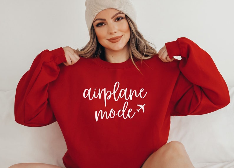 May include: A red sweatshirt with the words "airplane mode" in white script and a small airplane graphic. The long-sleeved top is a solid color and has a crew neck.
